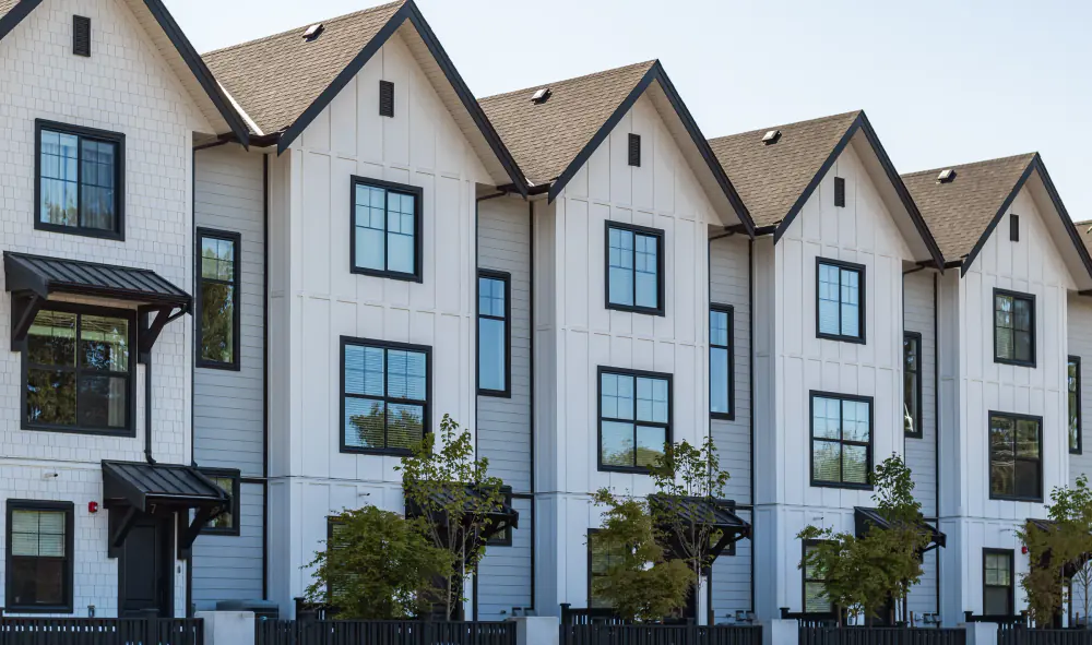 Row of white townhomes with black-trimmed windows and young trees out front